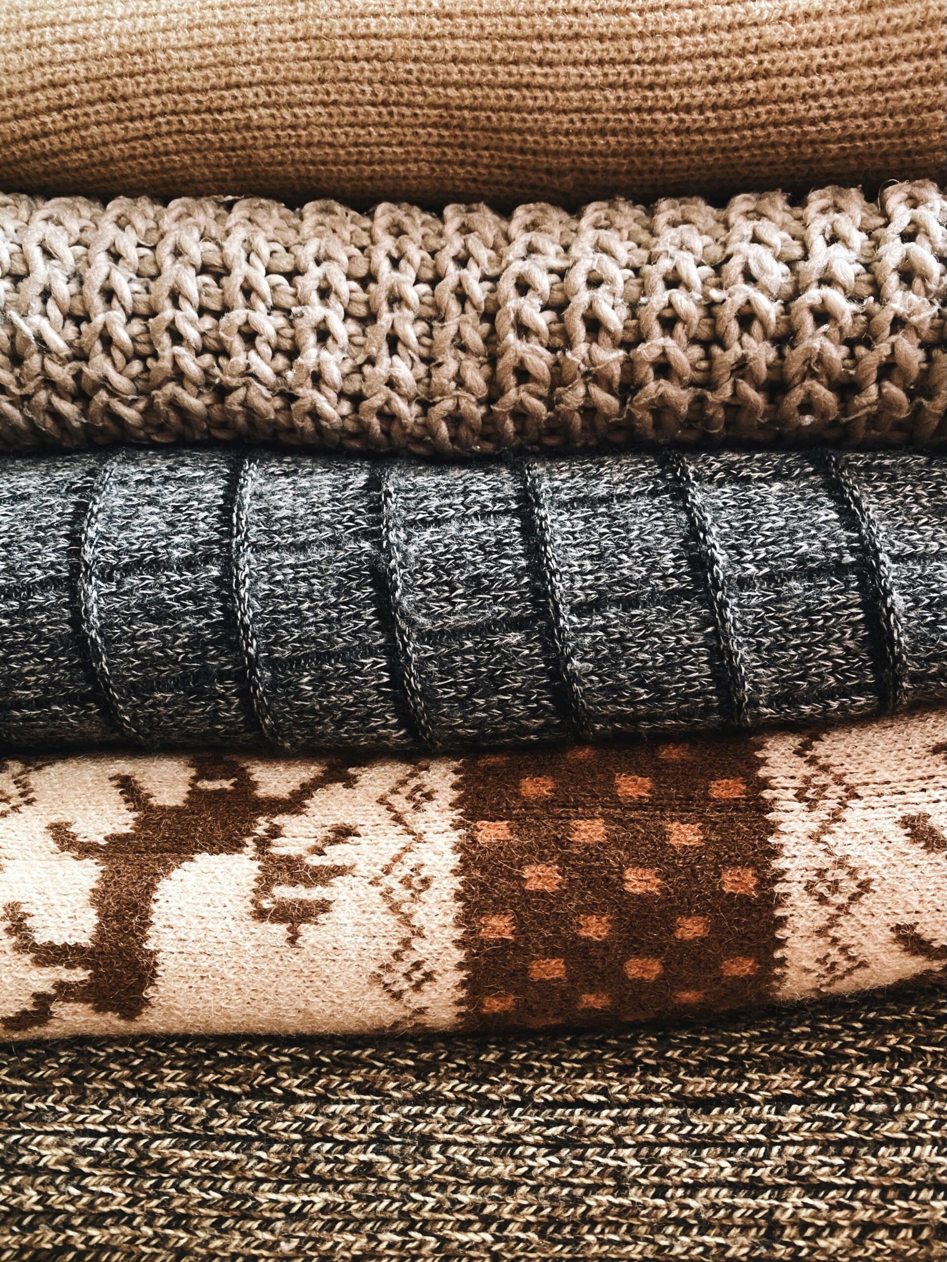 Stack of warm, knitted wool textiles showcasing intricate patterns and textures, perfect for cozy decor or fashion.